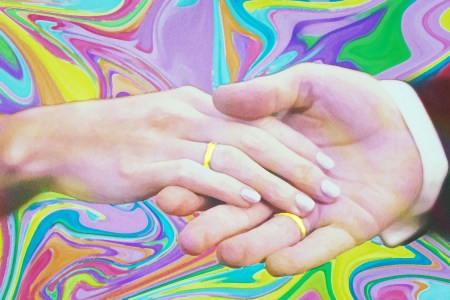 Hands with wedding rings clasped against a colorful background