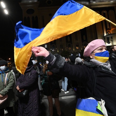 A woman wearing a face mask with the colors of the Ukrainian flag and waving a flag of Ukraine