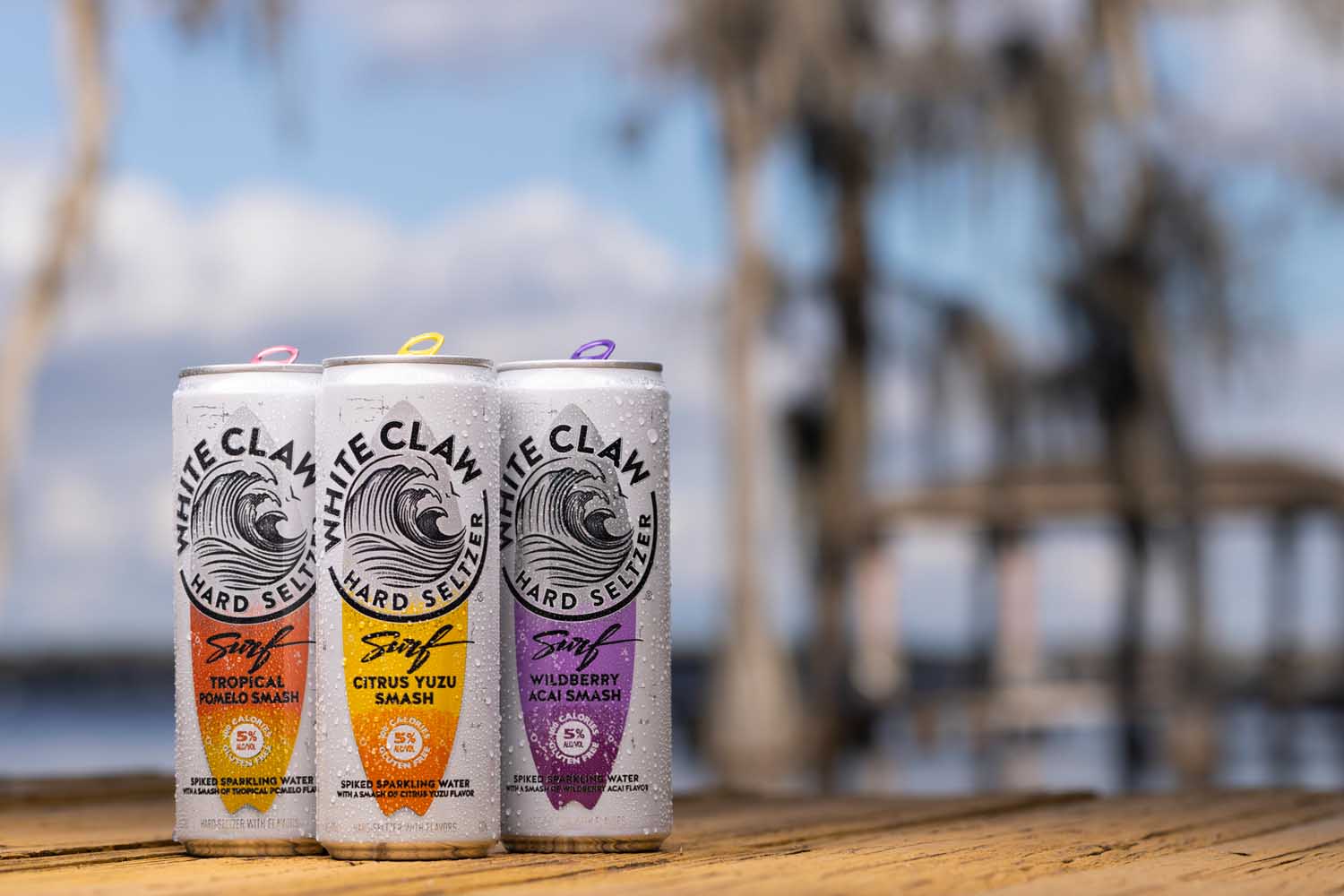 Three cans of White Claw Surf on a beach.