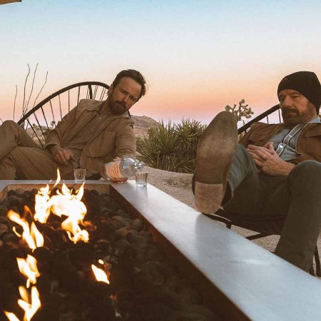 Dos Hombres mezcal owners Aaron Paul and Bryan Cranston drinking mezcal on a porch in front of a fire pit