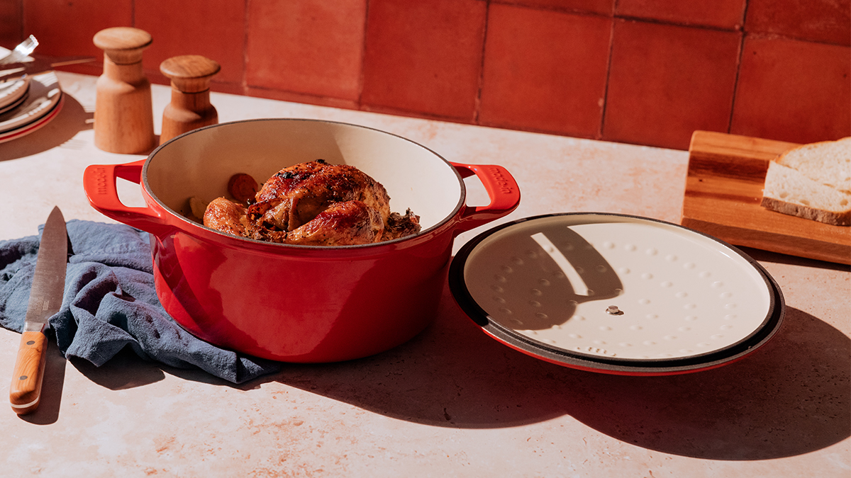 A red Dutch oven from the brand Made In sitting on a table with a chicken in the pot. We reviewed the enameled cast-iron Dutch oven and compared it to Staub and Le Creuset.