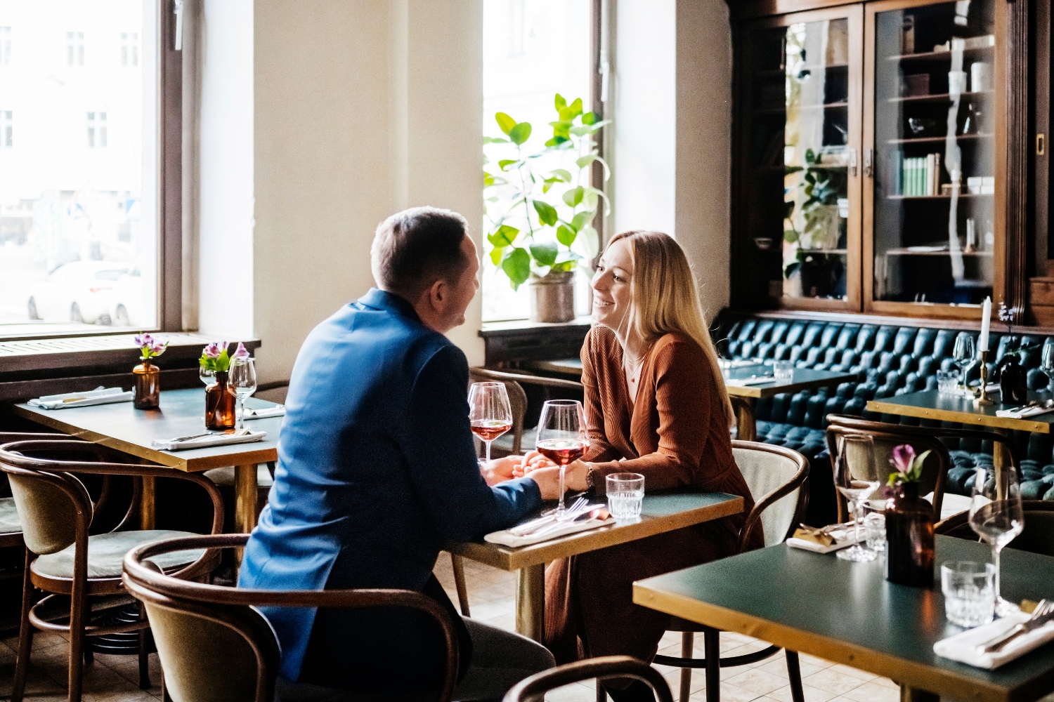 A couple holding hands while sitting down at a table and drinking red wine in a restaurant for lunch together,