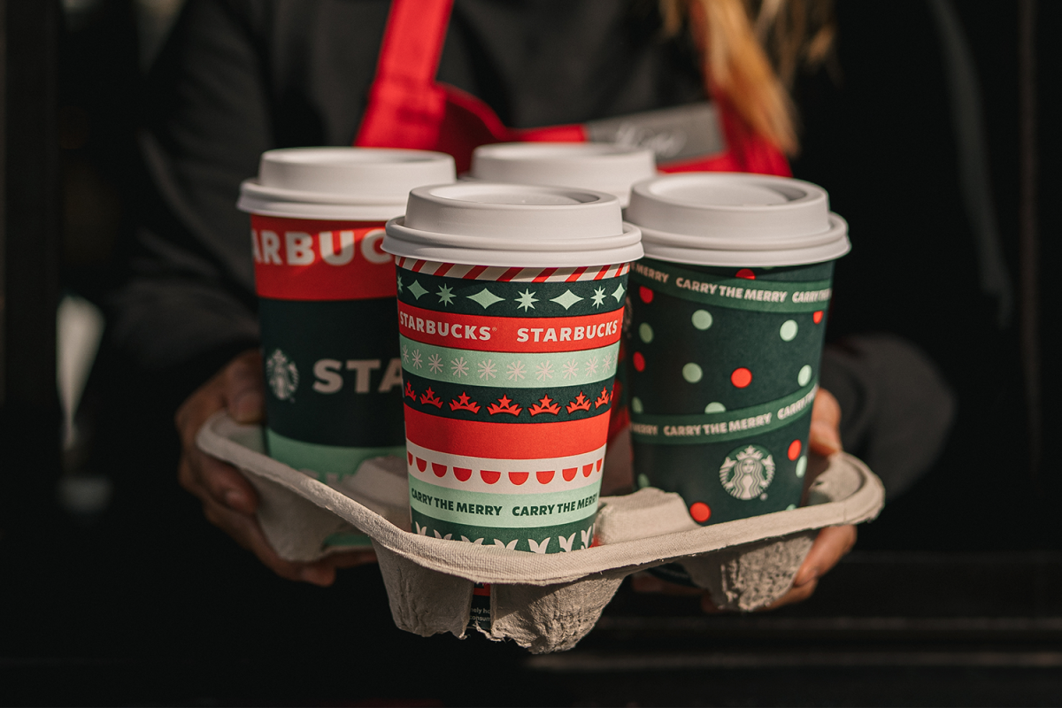 A Starbucks employee holding a tray of four Starbucks holiday cups. In March 2022 the company announced new reusable initiatives, not that it was eliminating disposable, single-use cups.