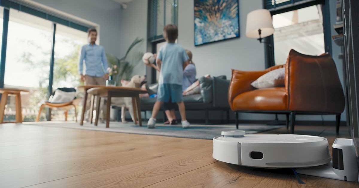 eufy RoboVac in action on a living room floor while a father and son play nearby. The RoboVacs are currently on sale at Amazon.
