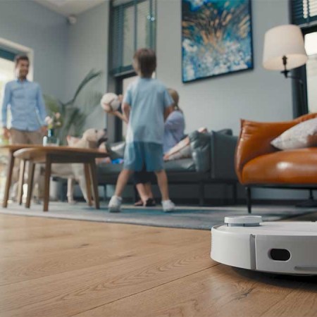 eufy RoboVac in action on a living room floor while a father and son play nearby. The RoboVacs are currently on sale at Amazon.