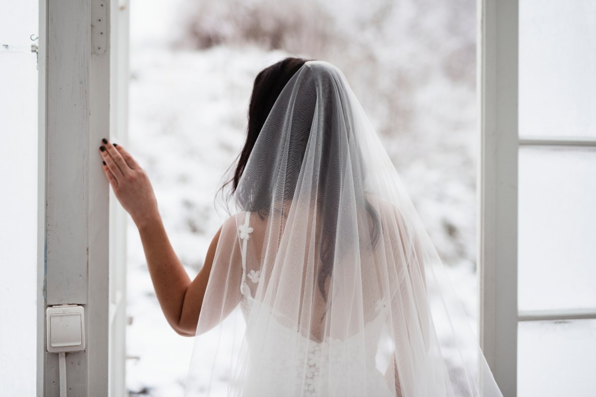A bride faces away from the camera looking out a window