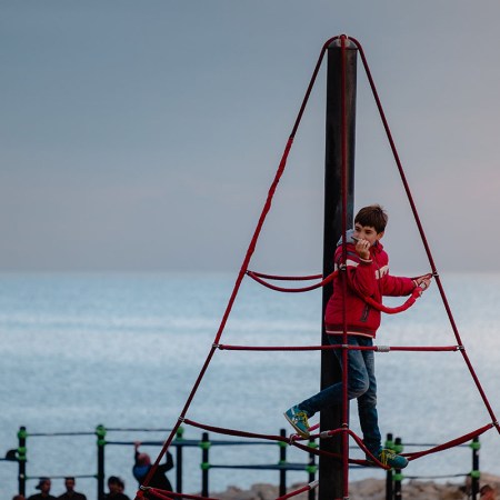 A boy on a playground near the ocean. This is an example of "risky play," but is it right for your kid? Parents are fighting about it online.