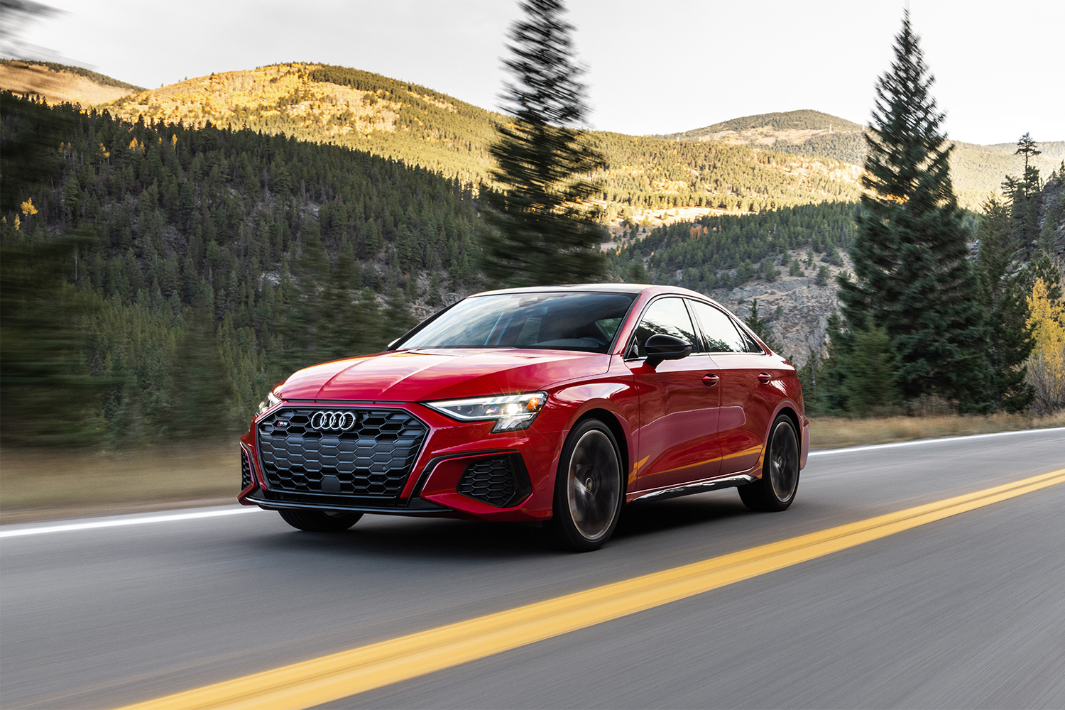 The 2022 Audi S3 in red driving along a two-lane road with hills and trees in the background