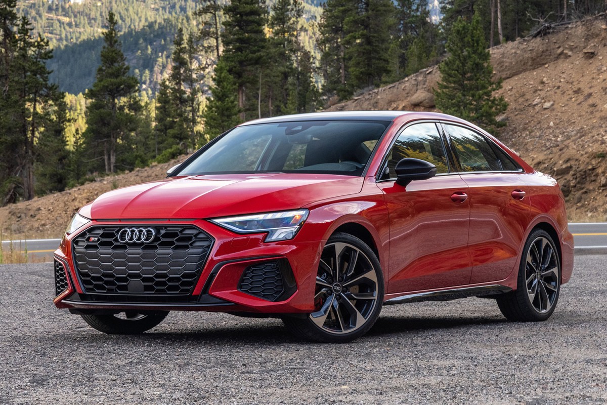 The 2022 Audi S3, a performance sedan, sitting still on a gravel area with forested mountains rising in the background. We tested and reviewed the sedan, and highly recommend it.
