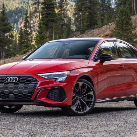 The 2022 Audi S3, a performance sedan, sitting still on a gravel area with forested mountains rising in the background. We tested and reviewed the sedan, and highly recommend it.