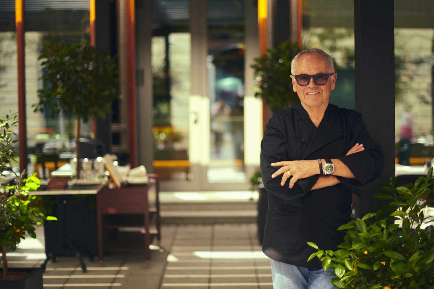 Wolfgang Puck lleva gafas oscuras y se cruza de brazos en el nuevo restaurante Spago Budapest.