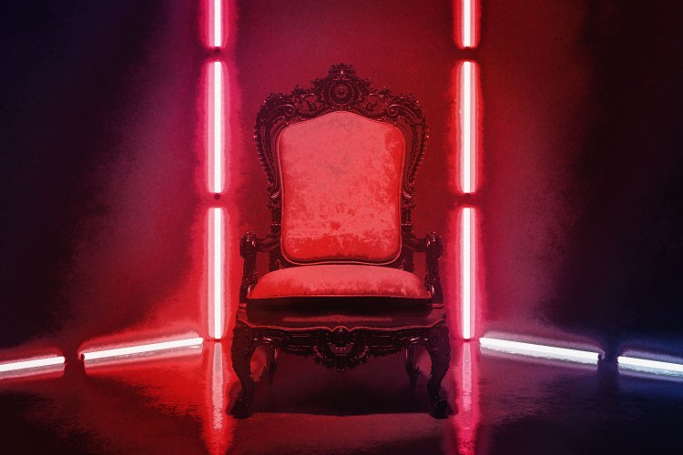 An empty, throne-like chair is illuminated by vibrant red lights.