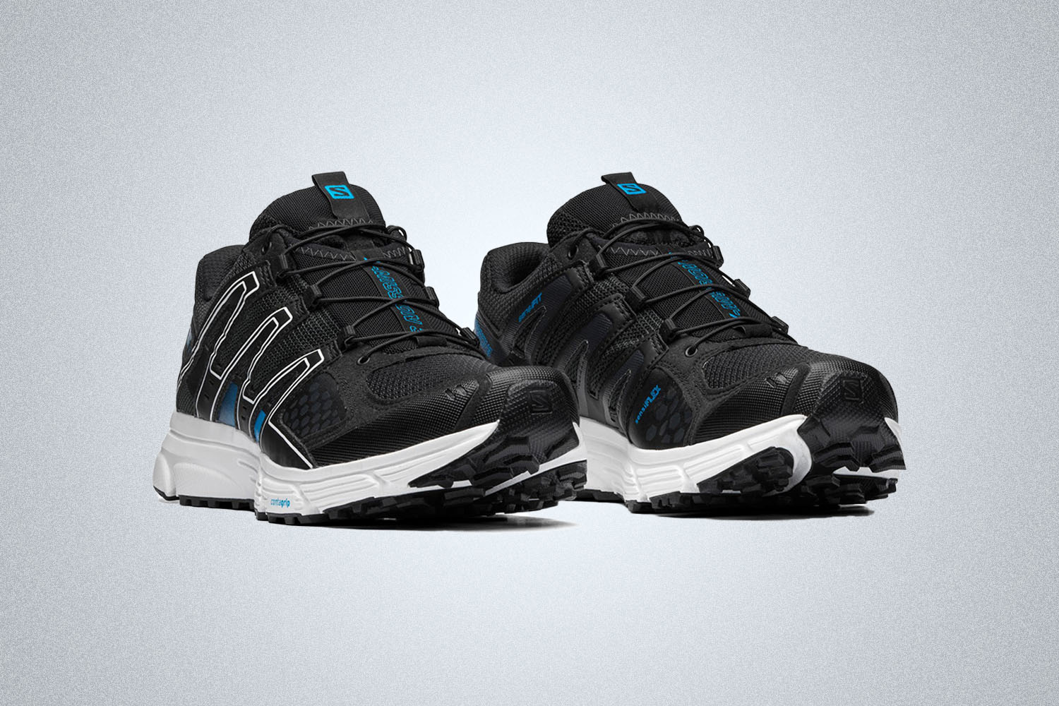 a pair of black Salomon hiking sneakers with white soles and blue accents on a grey background