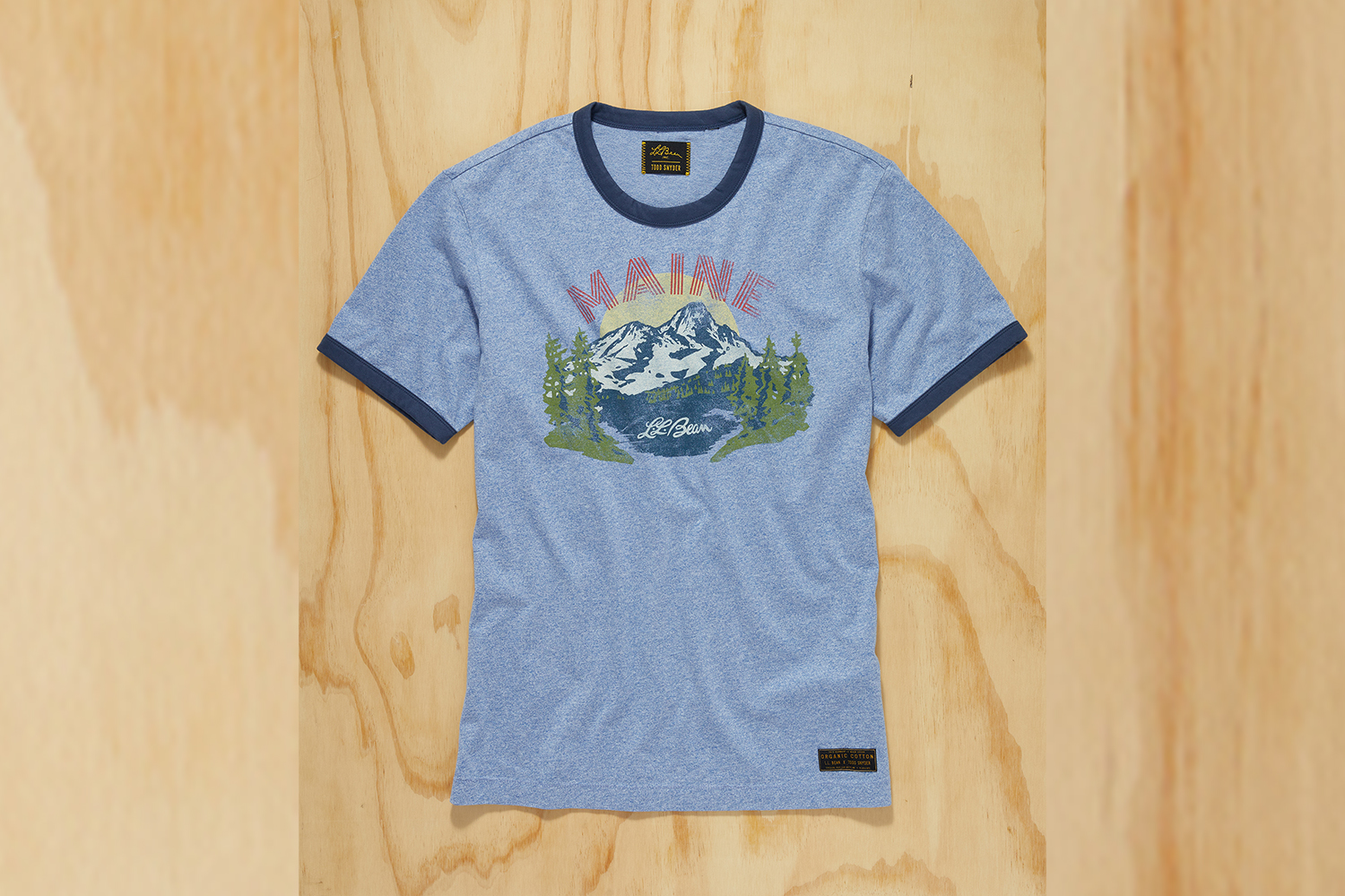 a blue ringer tee with Maine graphic on a wood background