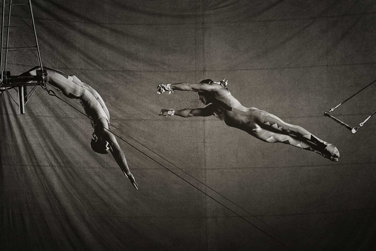 A black and white photo of two people performing trapeze