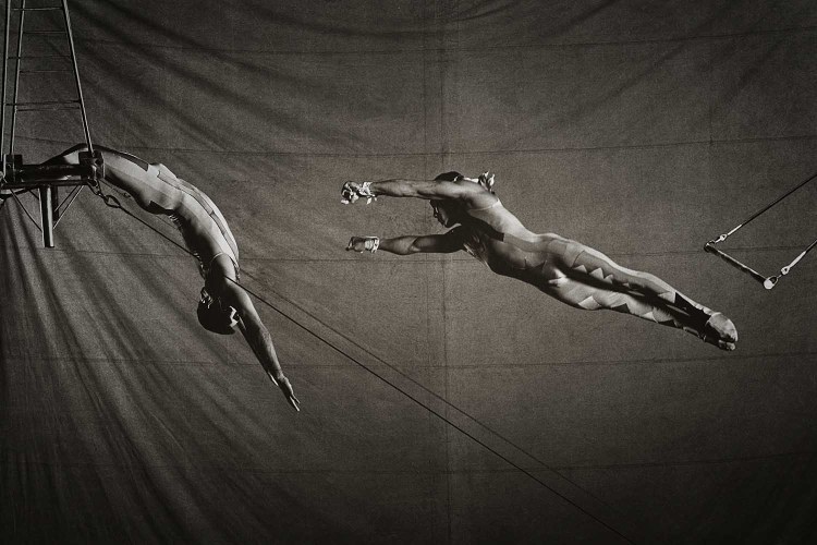 A black and white photo of two people performing trapeze