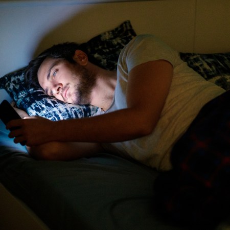 Young man lying in bed at night and using his smart phone