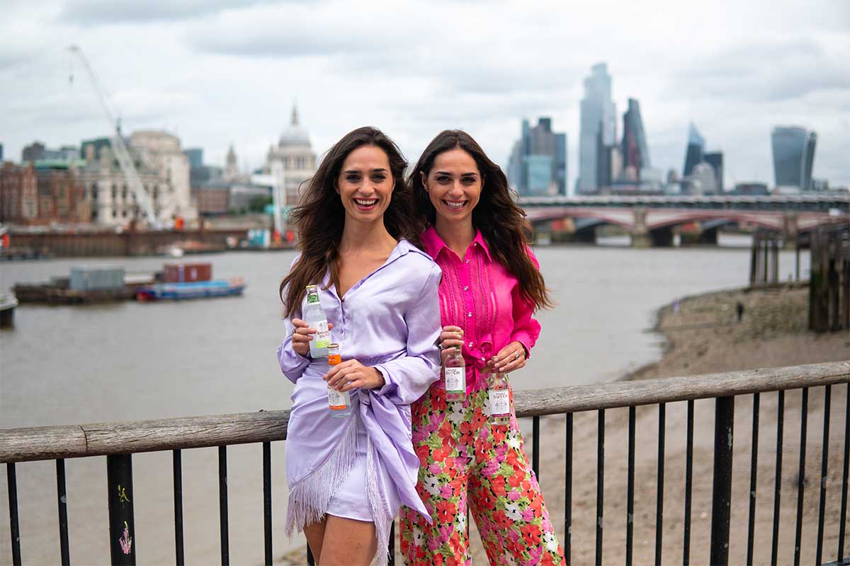 Double Dutch founders Joyce & Raissa De Haas, standing on a bridge with their new line of mixers, with London in the background