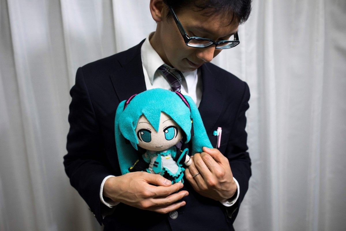 In this photograph taken on November 10, 2018 Japanese Akihiko Kondo poses with a doll of Japanese virtual reality singer Hatsune Miku, as both wear their wedding rings, at his apartment in Tokyo, a week after marrying her. Kondo is one of thousands of fictosexuals. Here's what you need to know about fictosexuality.