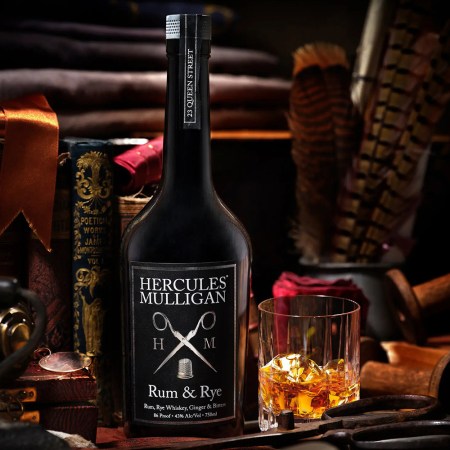 A bottle of the new rum/rye Hercules Mulligan near a drinking glass. We reviewed the drink and found it works best as a base spirit.
