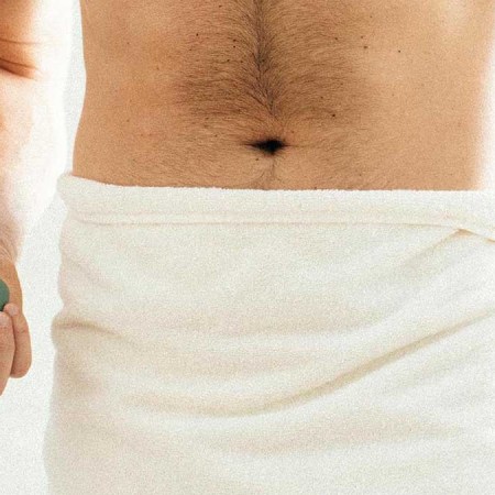 A man in a towel holding the Trimmer by Meridian, an electric shaver for "down there"