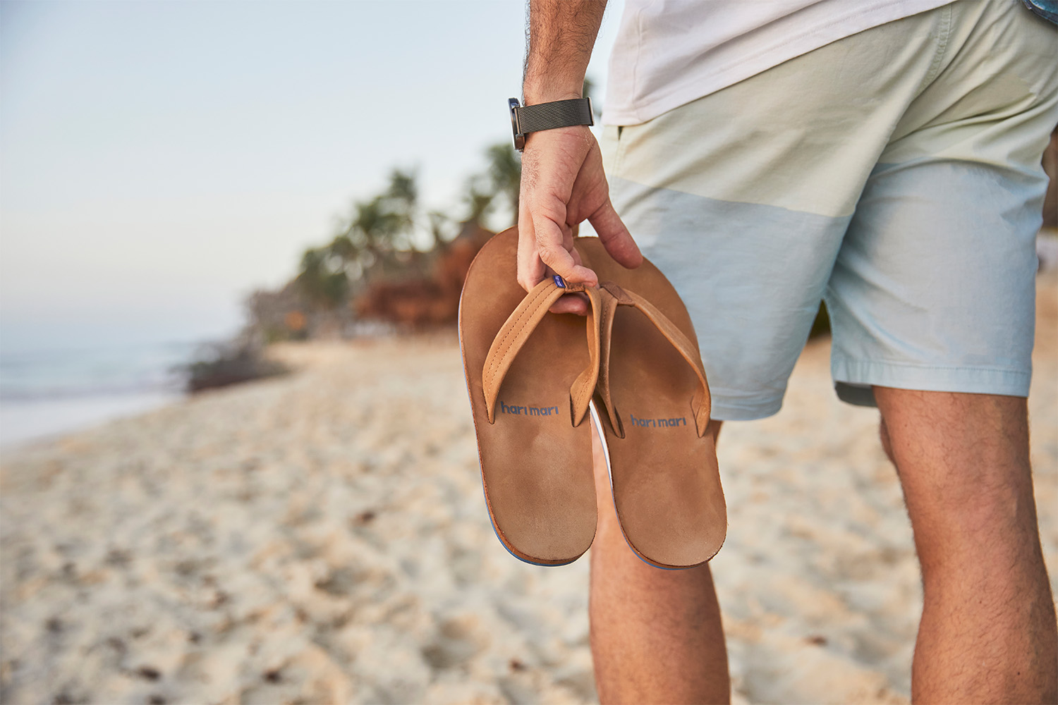 A man carrying a pair of Hari Mari sandals on the beach. We caught up with co-founder Lila Stewart to talk about the company's 10-year anniversary in 2022.