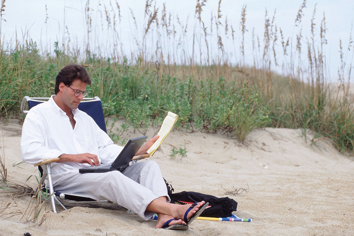 A man sitting with his laptop on the beach.