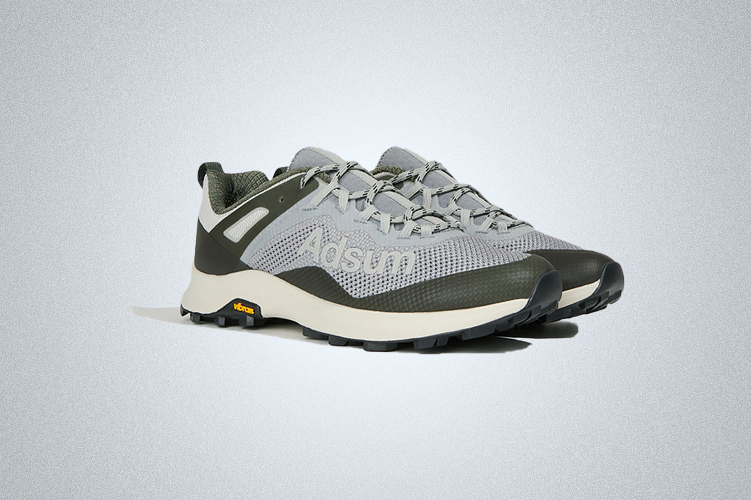 A pair of gray Merrell trail running shoes with Adsum branding on a gray background