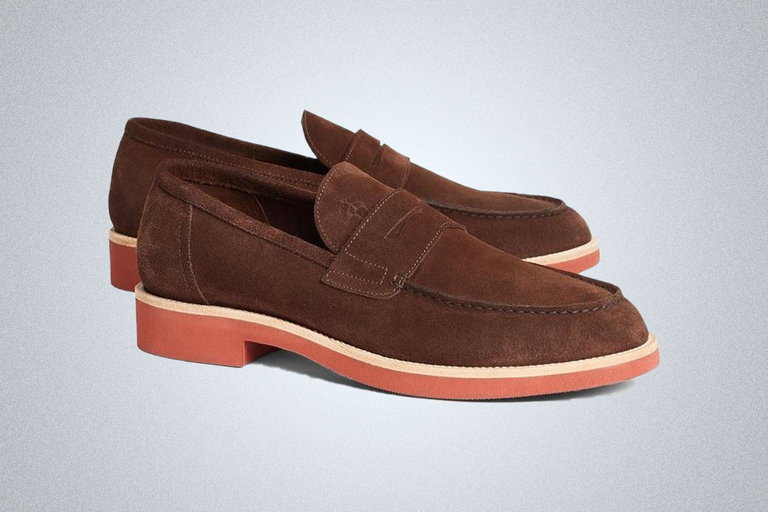 A pair of brown suede and red-soled penny loafers from Brooks Brothers on a grey background