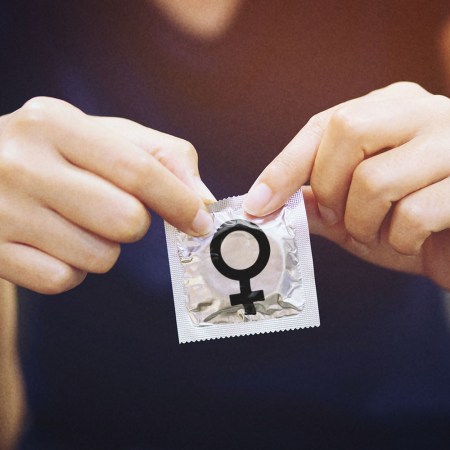 Close up photo shows a person opening a condom wrapper with a female symbol on it