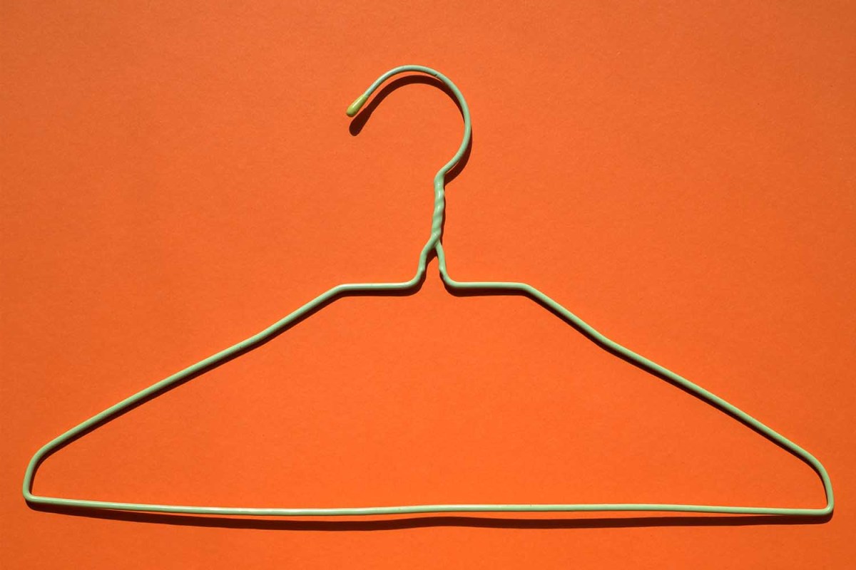 A light green clothes hanger on an orange background.