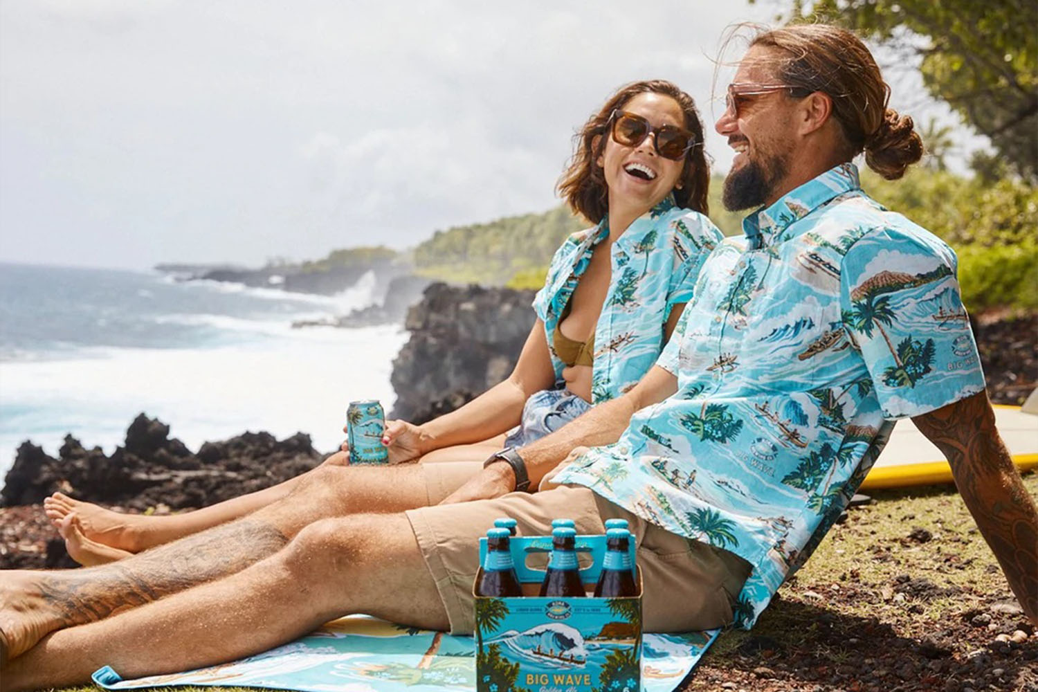 Two models wearing the Kona Brewing Aloha shirt on a towel with a pack of beer