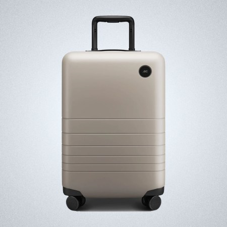a tan carry-on suitcase from Monos on a grey background