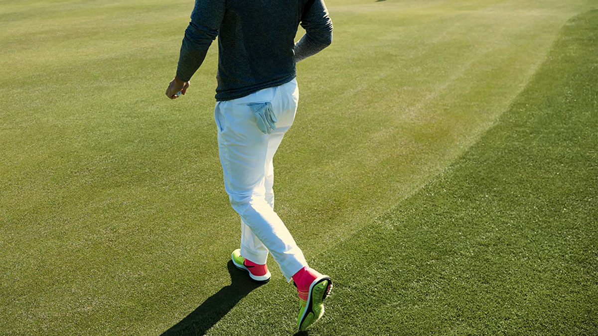 a Nike model on a golf fairway in a blue long-sleeve top and white pants with neon and pink Nike golf shoes