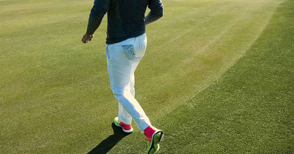 a Nike model on a golf fairway in a blue long-sleeve top and white pants with neon and pink Nike golf shoes