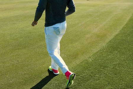 a Nike model on a golf fairway in a blue long-sleeve top and white pants with neon and pink Nike golf shoes
