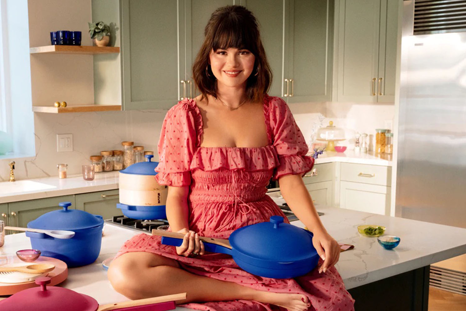 A campaign shot of Selena Gomez in a kitchen holding a blue Always Pan from Our Place