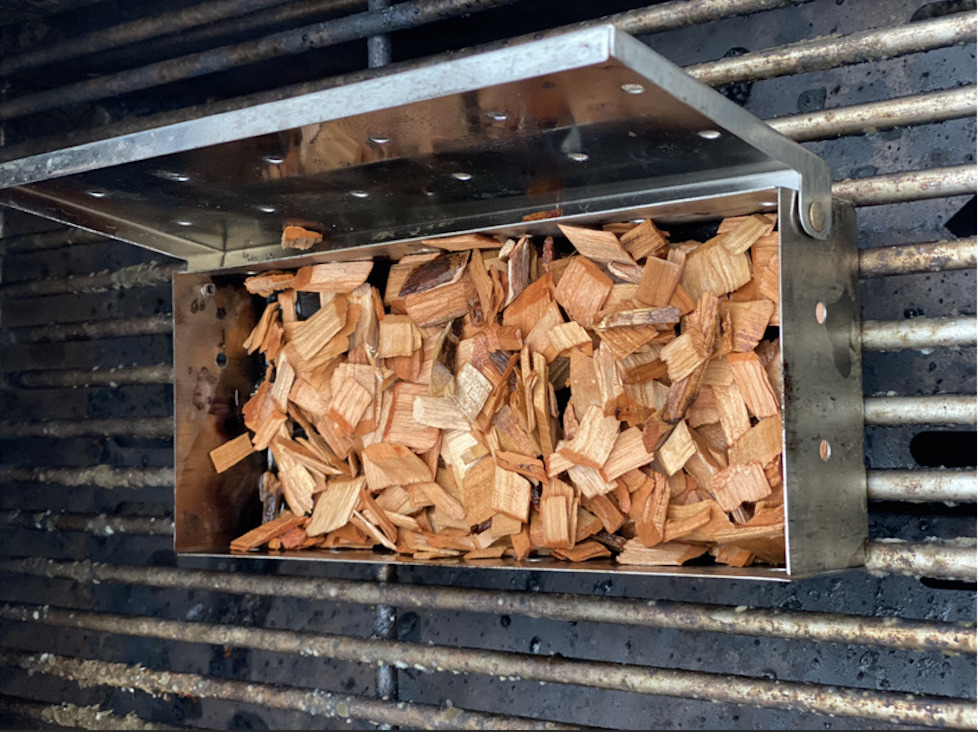 A smoke box filled with wood chips sitting on a grill.