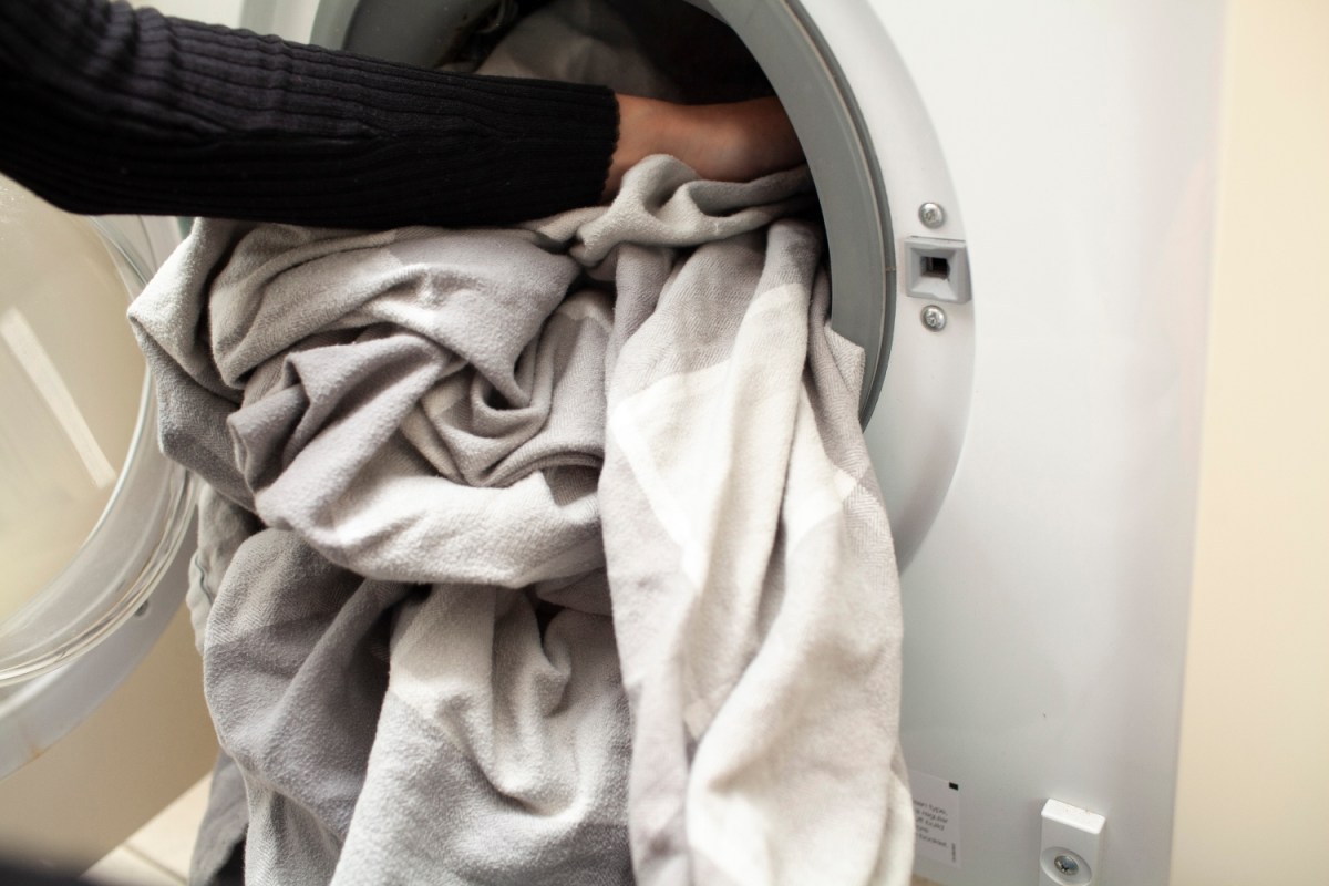 Close-up of hands loading bed sheets into a washing machine