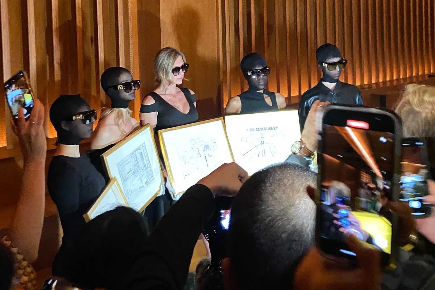 Models pose for photos holding Anna Delvey's sketches at her art show in NYC