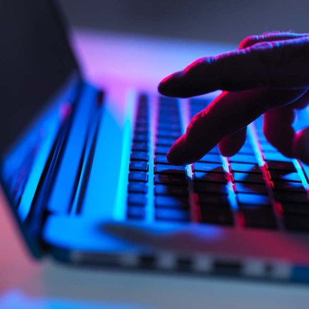 Silhouette of male hand typing on laptop keyboard at night - stock photo
