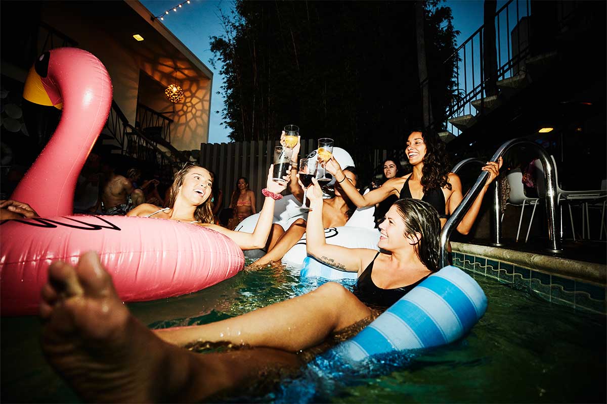 Female friends toasting while floating in hotel pool during party - stock photo