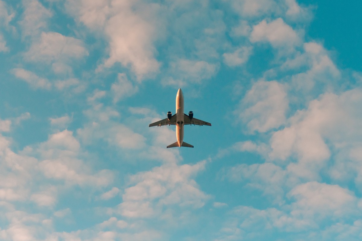 An airplane flying overhead in a blue sky. We take a look at the new features available in Google Flights and Google Travel more broadly.