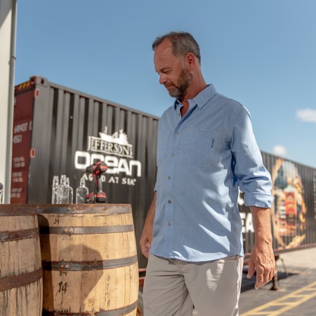 Jefferson's Bourbon founder Trey Zoeller stands next to a few barrels topped with bottles of his brand's whiskey. We spoke with Zoeller to get a local's guide to Louisville, Kentucky ahead of the Kentucky Derby.
