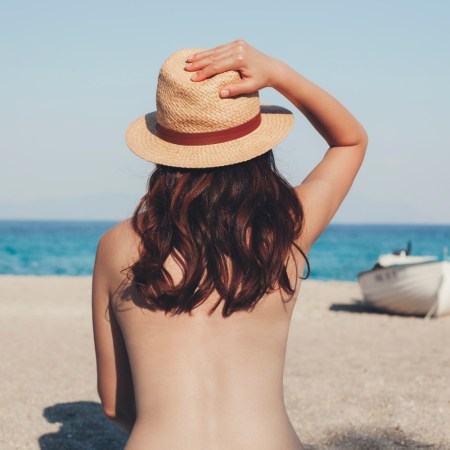 Topless young woman looking at the sea during summertime on the beach.
