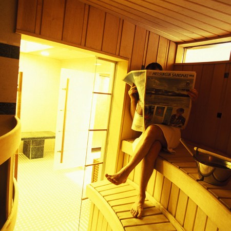 A Finnish man reads a newspaper in a sauna.