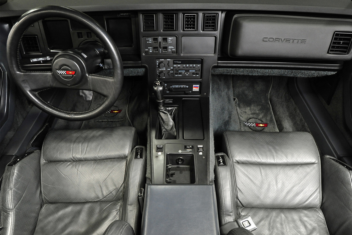 The interior of a 1986 Chevrolet Corvette C4 with black throughout and the Corvette logo on the steering wheel