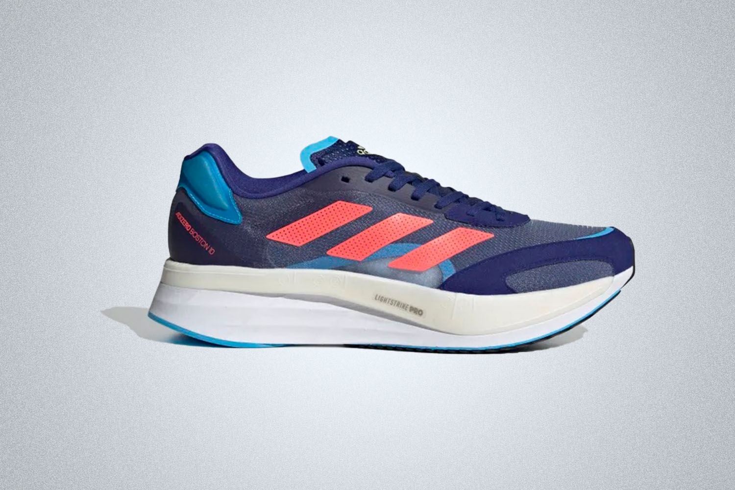 a pair of blue Boston 10 running shoes with red accents and a large white sole from Adidas on a grey background