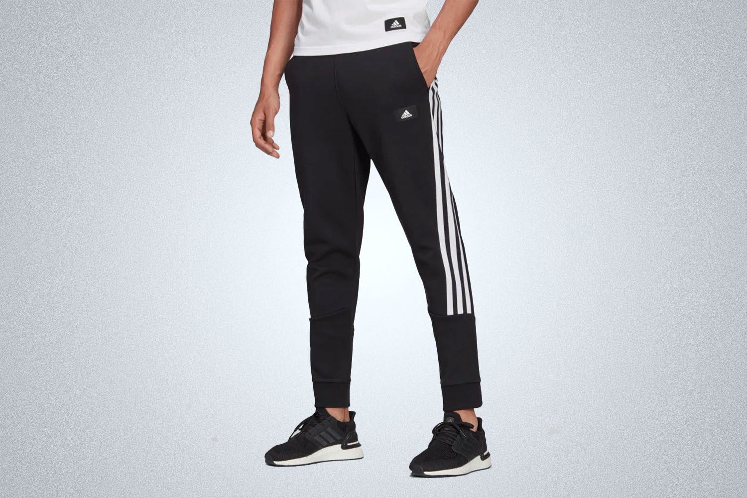 a model in a pair of side-striped black Adidas joggers from Adidas on a grey background