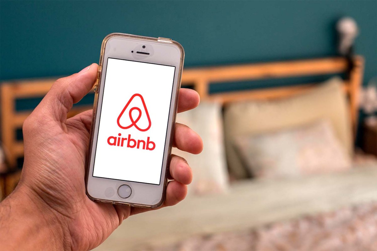 An Airbnb app as it appears on a mobile phone, with a bed in the background
